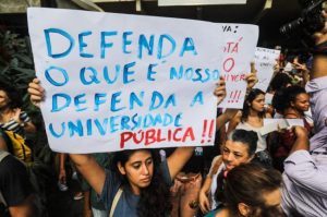 Grupo de pessoas em protesto, uma delas segura cartaz que diz: "Defenda o que é nosso, defenda a universidade pública"