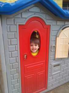 Criança feliz sorrindo por uma janela de uma casinha de brinquedo.