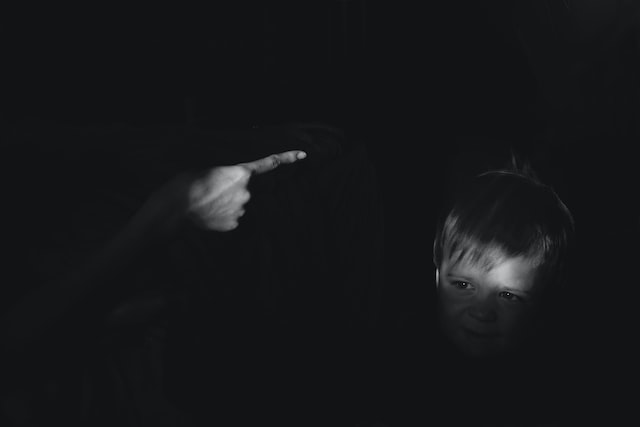 Foto em preto e branco mostra criança com rosto tenso ao ouvir um adulto gritando com ela, apontando o dedo em sua direção.
