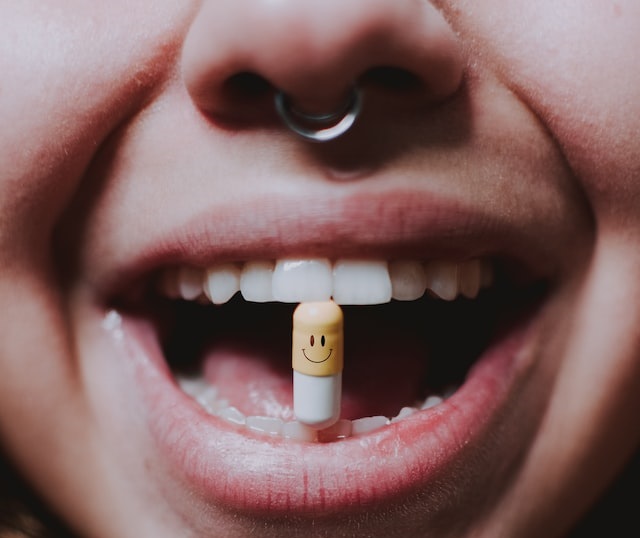 Foto mostra boca de adolescente, que usa piercing no nariz, que está prestes a tomar um medicamento antidepressivo.