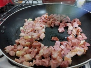 Bacon, calabresa e alho, picadinhos, refogando na frigideira.