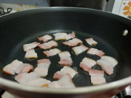 Pedacinhos de bacon fritando na frigideira.