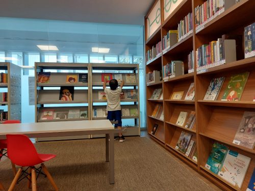 Menino pegando livro em estante de biblioteca.