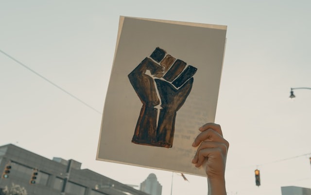 Cartaz mostra desenho de punho cerrado, ou punho erguido, usado historicamente como símbolo de resistência contra a violência, contra o fascismo e contra o racismo.
