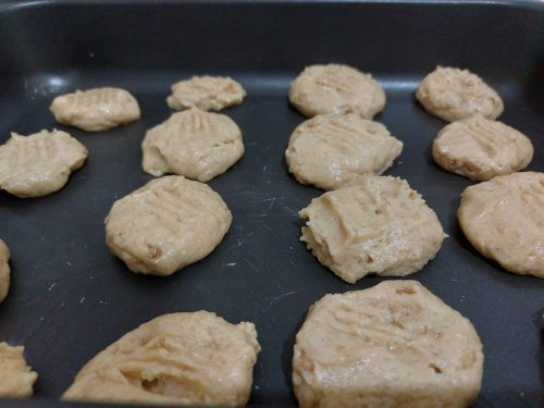 Biscoitos de nozes ainda crus, na assadeira, prontos para ir ao forno pré-aquecido.