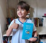 Luiz segura seu livro 'Viagem em Busca de uma Casa' e faz um joia, feliz e sorridente.