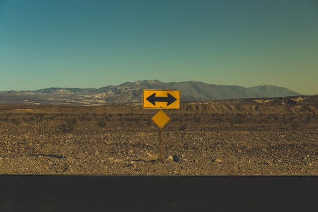 Placa com setas para os dois lados em meio a um deserto com montanhas. Foto: Pablo García Saldaña / Unsplash
