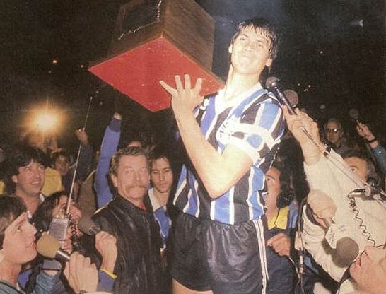 Mílton Jung (mais à frente, no canto esquerdo) aos pés de jogador do Grêmio que recebeu troféu do campeonato gaúcho, em 1987. Foto: Adolfo Gerchmann/revista Placar/ Editora Abril